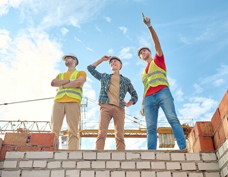 Men standing on brick wall of building under construction